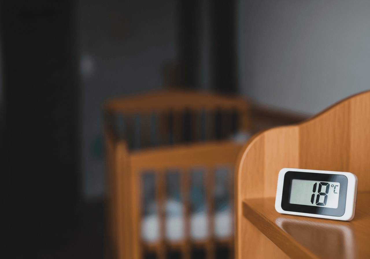 Digitales Raumthermometer auf 18 Grad im dunklen Kinderzimmer, die perfekte Schlaftemperatur bei Schlafproblemen beim Baby.