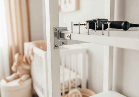 Wohnung baby-sicher machen: Metallwinkel zur Kippsicherung eines weißen Bücherregals an der Wand